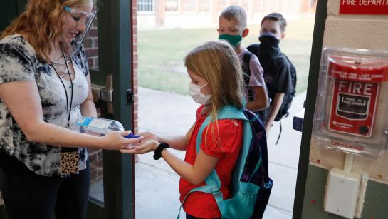 teacher and students practicing COVID-19 precautions before entering school