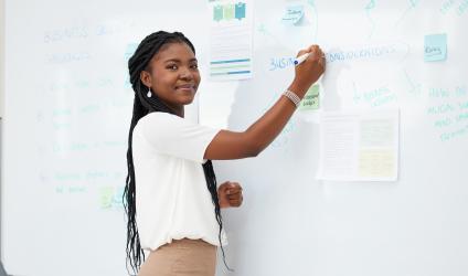 Person standing at a white board writing notes but looking towards camera