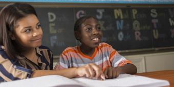 Female African American teacher working with young African American student on reading a text