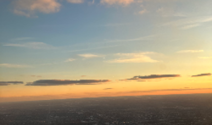 [image of the land and sky from an airplane window during sunset in mid-flight, with the plane engine included in the view] 