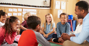 Young diverse male teacher sitting amongst young diverse students