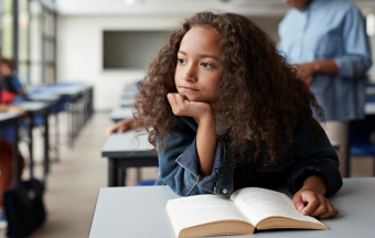 elementary school girl reading book at classroom desk